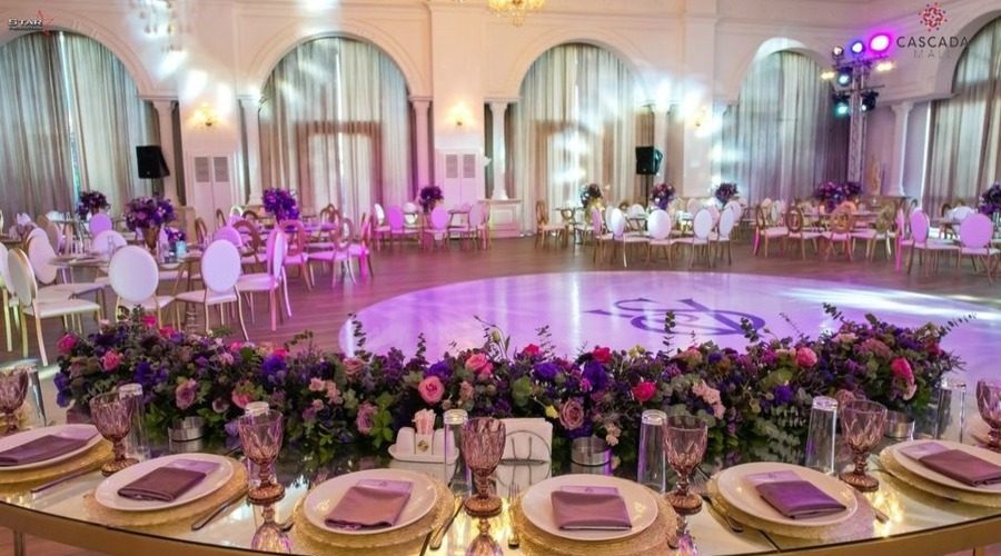 The ballroom set for a wedding, round tables in purple and gold around a lit dance floor