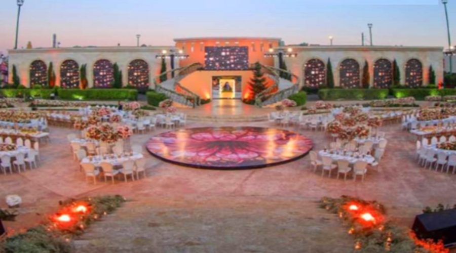 The outdoor arena set for a reception, arched wall behind the stage at dusk